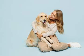 Full body cheerful lovely young owner woman wearing casual clothes sitting hug cuddle embrace her best friend retriever dog isolated on plain light blue background studio. Take care about pet concept.