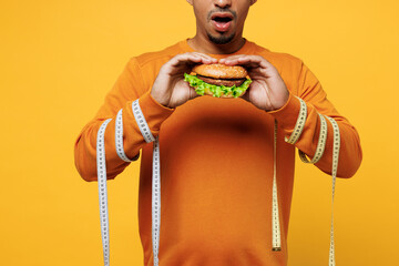 Close up cropped young man wears sweatshirt casual clothes eat burger with tied hands by measure...