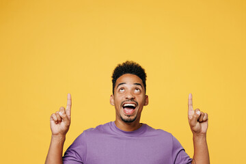 Young surprised man of African American ethnicity wears purple t-shirt casual clothes point index finger overhead on area mock up isolated on plain yellow background studio portrait Lifestyle concept - Powered by Adobe