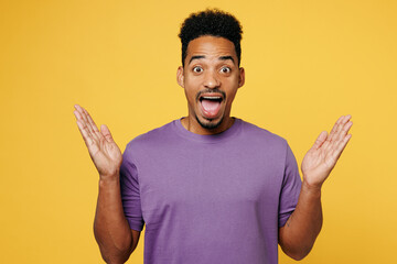 Young surprised shocked happy man of African American ethnicity he wears purple t-shirt casual clothes spread hands look camera isolated on plain yellow background studio portrait. Lifestyle concept.
