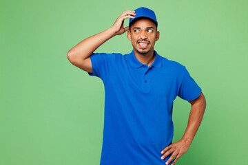 Professional mistaken confused delivery guy employee man wear blue cap t-shirt uniform workwear work as dealer courier look aside hold scratch head isolated on plain green background. Service concept.
