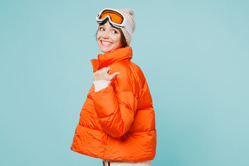 Skier young woman wear warm padded windbreaker jacket hat ski goggles mask point thumb finger back...