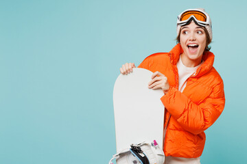 Young excited woman wear warm padded windbreaker jacket hat ski goggles mask hold snowboard look...