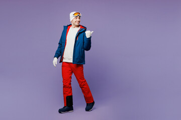 Full body skier man wear warm blue windbreaker jacket ski goggles mask hat walk go point finger aside blank area spend extreme weekend winter season in mountains isolated on plain purple background © ViDi Studio