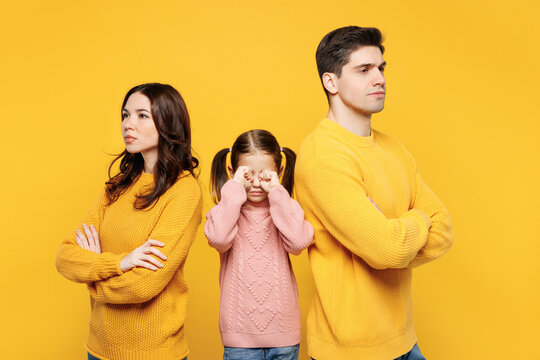 Young strict serious sad parents mom dad with child kid girl 7-8 years old wear pink knitted sweater casual clothes cover eyes with hands cry isolated on plain yellow background. Family day concept.