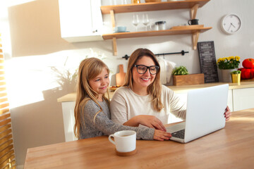 Mother with little girl using laptop in the kitchen