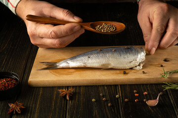 Cooking marinated fish Clupea with aromatic spices by the hands of a chef on a cutting board. Fish...
