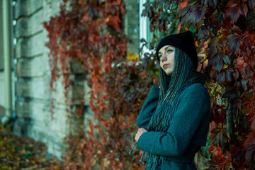 Fototapeta premium Portrait of a young beautiful girl with a smile on her face in an autumn park against a background of colorful leaves. A girl with dreadlocks and pigtails poses against the background of trees.