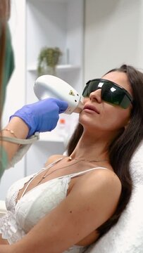 Beauty master makes laser hair removal epilation of lips close-up in a beauty salon for a girl in glasses with beautiful pricked lips