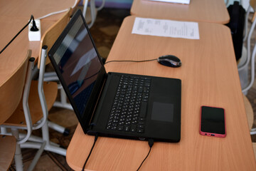 A black laptop and a phone on the desktop. An office workplace with a computer.
