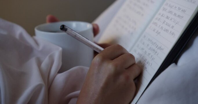 Person, hands and writing in book with coffee for story, literature or reading on bed at home. Closeup of writer or journalist taking notes in diary, notebook or paragraph for paperwork in bedroom