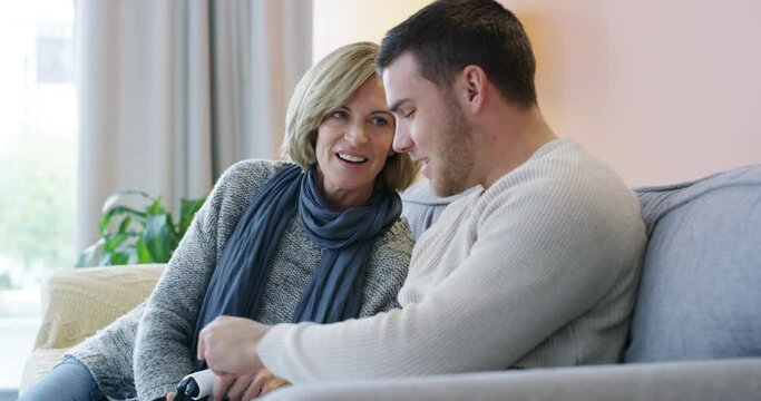 Young man, mother and sofa teaching controller buttons for video games or bonding in living room together at home. Happy male person, son and showing mom controls for console gaming
