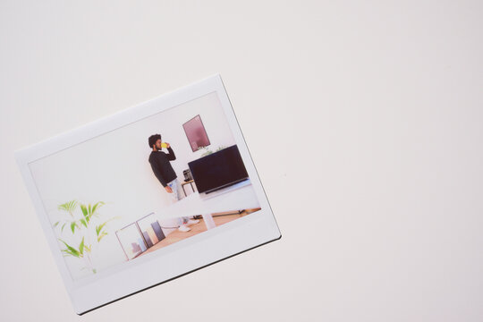 single Polaroid photo depicting a serene morning moment as a young man enjoys a cup of coffee while standing in a modern living space, with contemporary tech and decor subtly framing the scene.