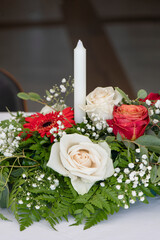 Floral candleholder designed for the the dinner table at a special event or wedding, flowers arrangement with white, cream and vibrant dark orange roses, popping red gerbera daisies and lush greenery