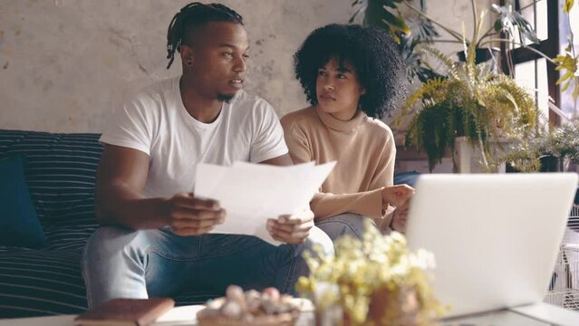 Black couple, laptop and documents in financial debt, budget planning or expenses on sofa at home. African man and woman with paperwork on computer for finance, bills or invoice together at house