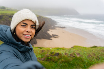 Latina woman with knit hat enjoying a beautiful views of the wild Irish coast on a windy day