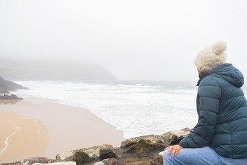 Unknown woman with her back looking a completely lonely beach with rough waves and fog in Ireland...