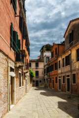 Narrow street of Murano with colorful houses and plants in early morning in Venice.