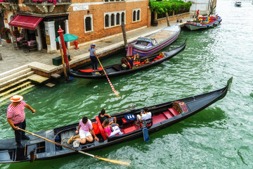 Venetian gondolier punting gondola through green canal waters of Venice. - obrazy, fototapety, plakaty