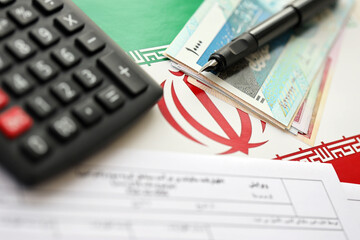 Iranian annual income tax return form F20-25-006 ready to fill on table with pen, calculator and iranian money on flag close up