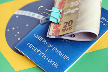 Brazilian work card and social security blue book and reais money bills on flag of Federative Republic of Brazil close up - obrazy, fototapety, plakaty