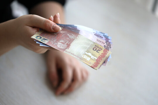 Brazilian money bills in woman hand. Female gives bunch of brazilian reais to us close up