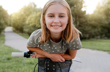Cute preteen girl with bycicle outdoors looking at camera and smiling. Pretty child with bike at...