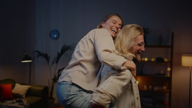 Funny boyfriend holding girlfriend on his back in apartment