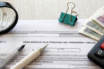 Declaration for tax on goods and services VAT-7 form on accountant table with pen and polish zloty money bills close up