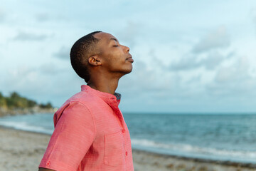 Young adult black man breathing fresh air on the beach	
