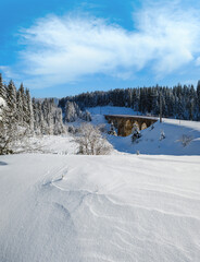 Stone viaduct (arch bridge) on railway through mountain snowy fir forest. Snow drifts  on wayside and hoarfrost on trees and electric line wires.