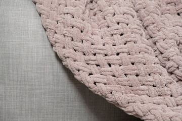 Knitted large plaid blanket in dusty rose light grayish-red color on the sofa.