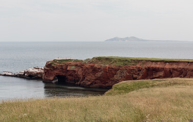 vue sur la côte avec une falaise de roche rouge recouverte de gazon verte en été lors d'une journée grise