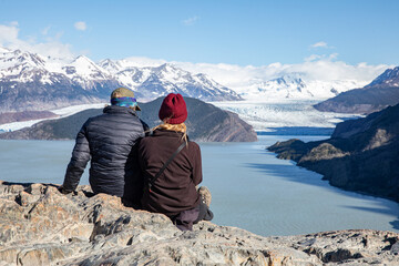 Two people sitting on a rock looking away to Patagonia landscape with mountains, clouds, glaciers,...