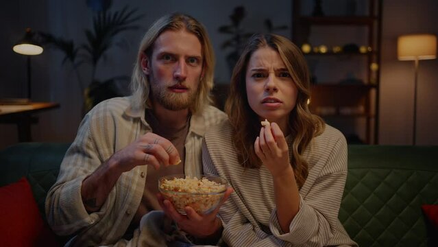 Tensed couple eating popcorn and getting scared by horror