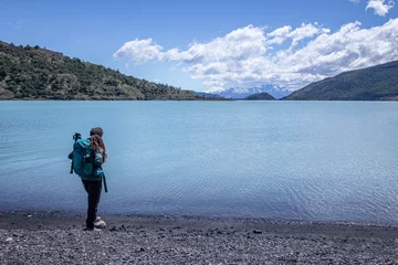 Photo sur Plexiglas Alpamayo A female hiker standing on a stone beach looking away to Patagonia landscape with mountains, clouds, glaciers, and a blue lake