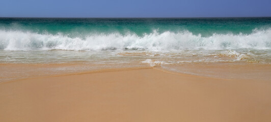 A  wave with turquoise water and white foam approaches on a windy day at Boa Vista's beach, Cape Verde.