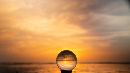 Colorful yellow, orange sunrise at the beach, reflected in crystal lens ball on a stand glass...