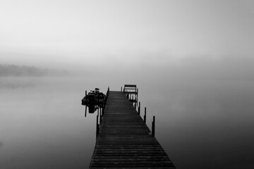 Foggy dawn at the dock with a fishing boat and bench at Lake Vermilion in northern Minnesota. Photo in black and white.