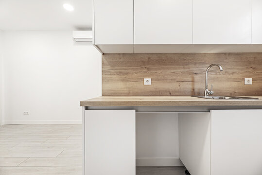 a kitchen with white cabinets and oak countertops with matching backsplashes in an empty loft style home