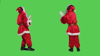 Santa claus using audio headset to listen to music and have fun during christmas eve holiday, full body greenscreen backdrop. Saint nick cosplay in costume dancing on songs, entertainment.