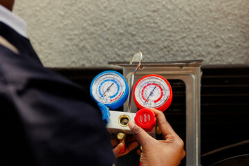 Pressure indicator tool able to find malfunctioning expansion valve and other issues, close up. Technician using manifold benchmarking gadget to read refrigerant levels of outdoor air conditioner