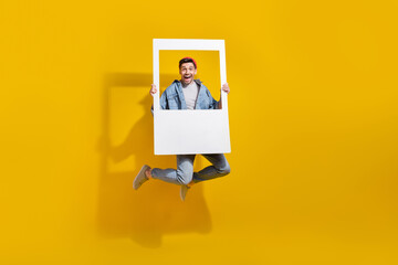 Full length photo of funky cheerful man dressed jeans shirt jumping high taking photo isolated yellow color background - obrazy, fototapety, plakaty