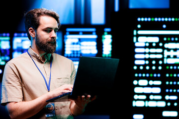System administrator using laptop to check high tech server rigs. Rackmounts in computer network...