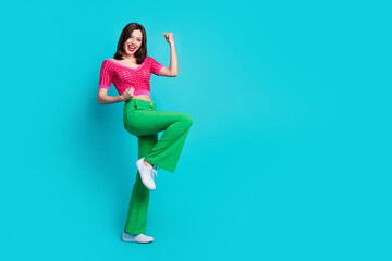 Full length photo of satisfied woman dressed top green pants scream yeah win betting clenching fists isolated on blue color background - obrazy, fototapety, plakaty