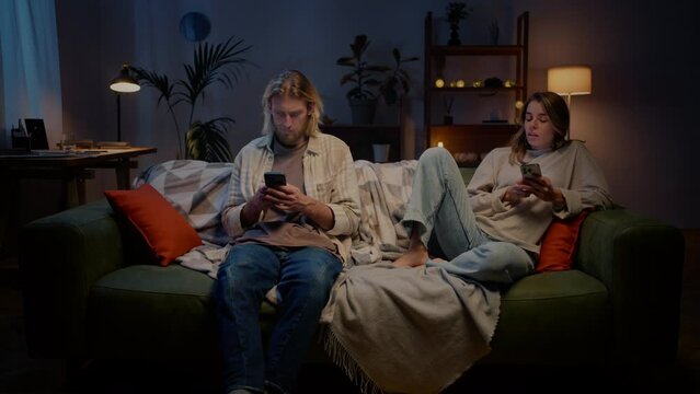 Couple sitting on sofa with phones and looking at each other