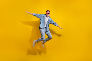 Fototapeta na wymiar Full length photo of good mood carefree man dressed jeans shirt dark spectacles jumping high isolated yellow color background