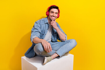 Photo of dreamy cheerful man dressed jeans shirt sitting white podium enjoying songs empty space isolated yellow color background