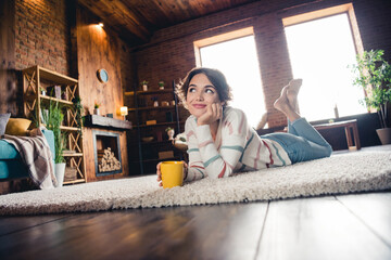 Full length photo of minded pretty person lying comfy carpet floor drink coffee inspiration...