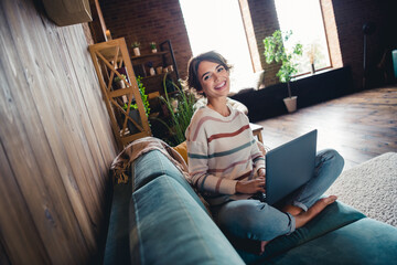 Full size photo of positive barefoot girl sitting sofa use laptop eshopping spacious modern flat...